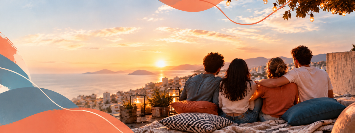 Four friends sitting together on cushions and blankets on a rooftop, watching the sunset over the sea and the city